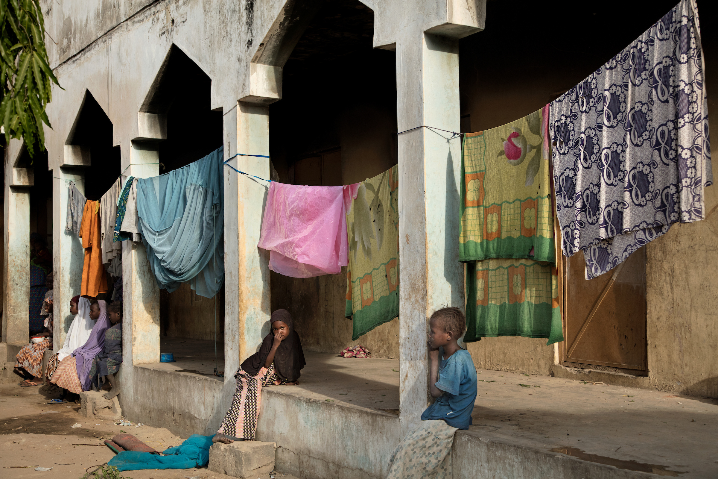 Girls sit beneath drying laundry in a makeshift refugee camp in Maiduguri, Nigeria.