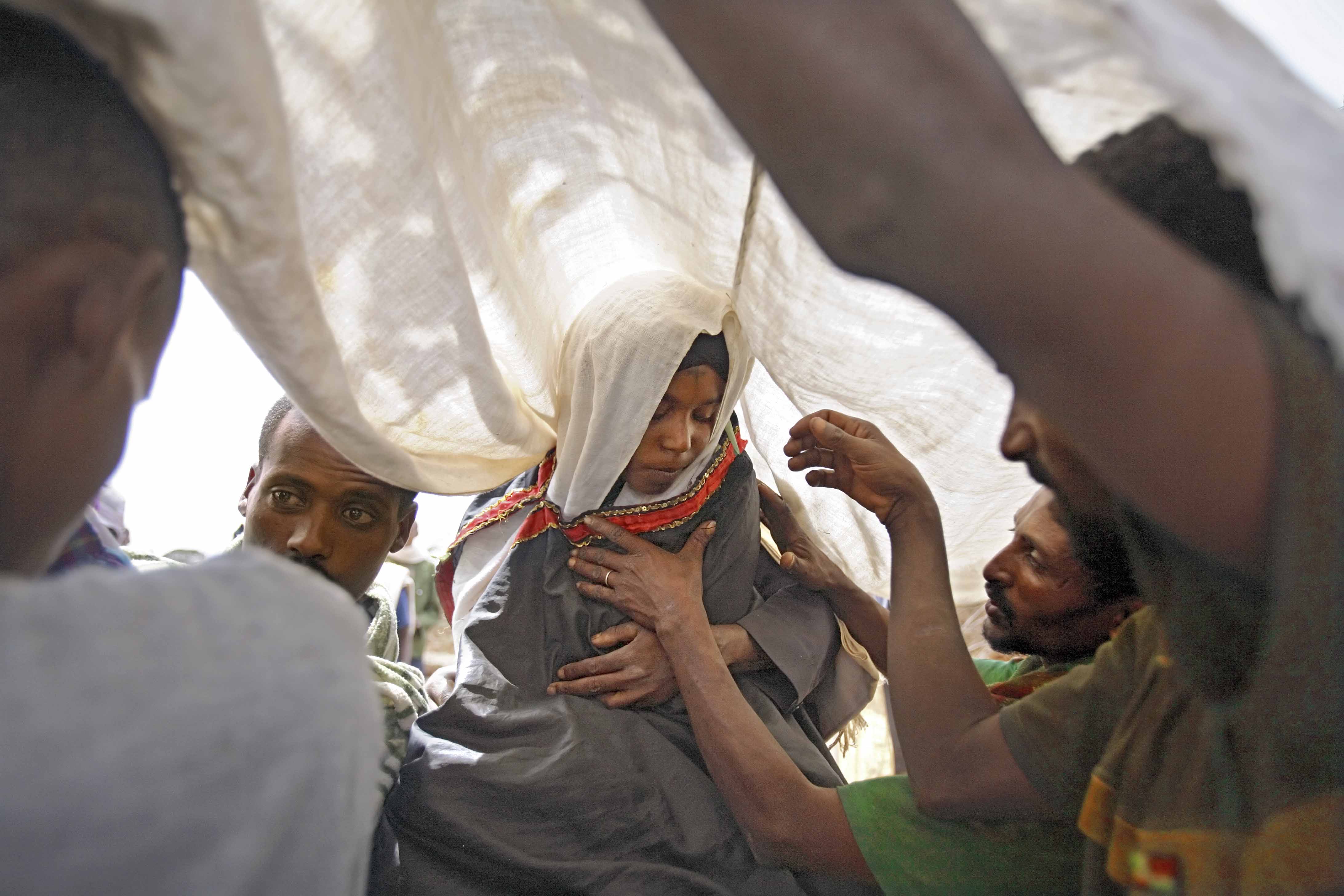 Family members place a white cloth over the head of Leyualem, 14, as she is prepared to be whisked away on a mule by her new groom and his groomsmen in Ethiopia.